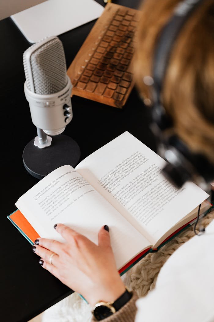 High angle of elegant female audiobook narrator recording audiobook while sitting at desk with microphone